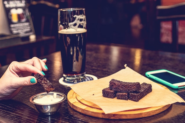 Plate of brownie pieces with a glass of dark beer in the background, and one brownie piece being dipped in cream