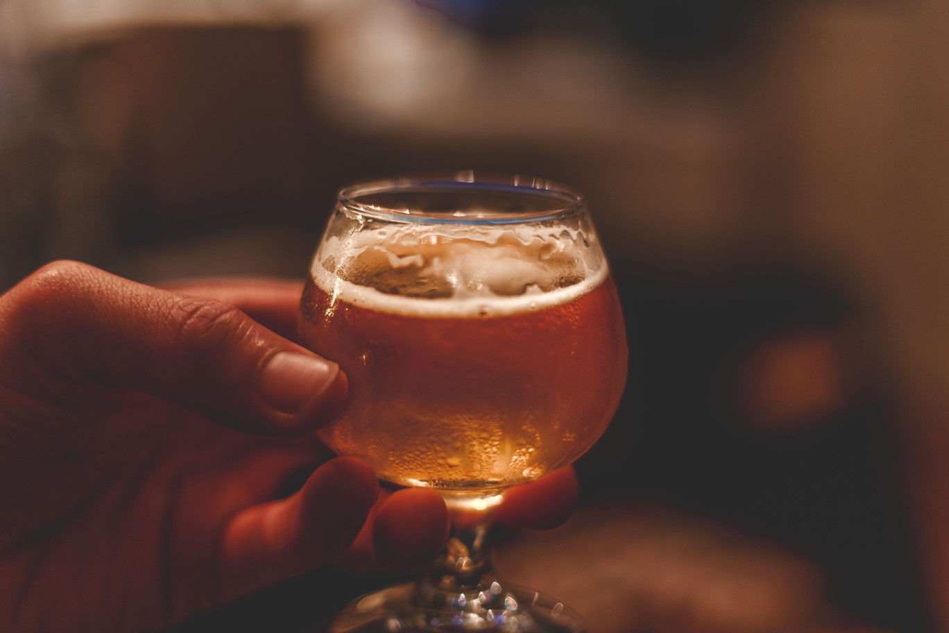 Hand holding a small wine glass of beer