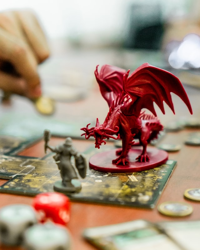 Close up of a board game, with a dragon miniature looming over a fighter miniature