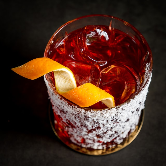 Red cocktail in a tumbler with a spiral of orange peel