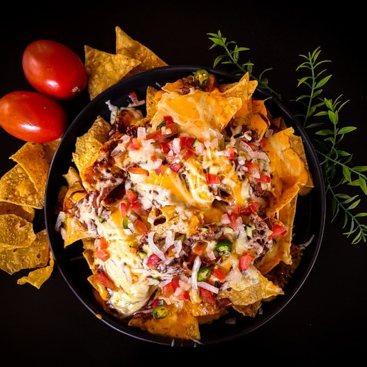 Overhead shot of a plate of nachos, decorated with tomatos, tortilla chips and sprigs of herbs
