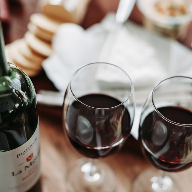 Two glasses of red wine on a table with a bottle and a cheese platter in the background
